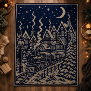 Könnte beinhalten: Eine marineblaue und beige gestrickte Decke mit einer Winterdorf-Szene. Das Design zeigt einen Zug, Häuser, Bäume, einen Mond und Sterne. Die rechteckige Decke ist wahrscheinlich aus weichem Material gefertigt, Abmessungen in Zentimetern.