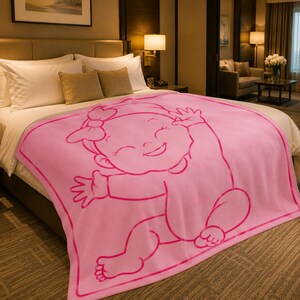 Pu&ograve; includere: Una coperta rosa per bambini con un disegno di un bambino sorridente. La coperta presenta un grande bambino sorridente con un fiocco, con le braccia alzate. La coperta &egrave; su un letto con lenzuola e cuscini bianchi.