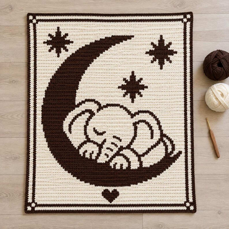 May include: A rectangular crochet blanket featuring a dark brown crescent moon and a sleeping elephant design on a cream background. The blanket is bordered by a dark brown frame with corner accents and includes three dark brown star motifs.