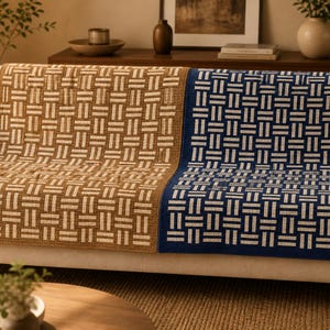 May include: A close-up of two woven throw blankets with geometric patterns. One blanket is tan and cream, the other is navy blue and cream. The blankets are draped over the back of a sofa, showcasing their texture and design.