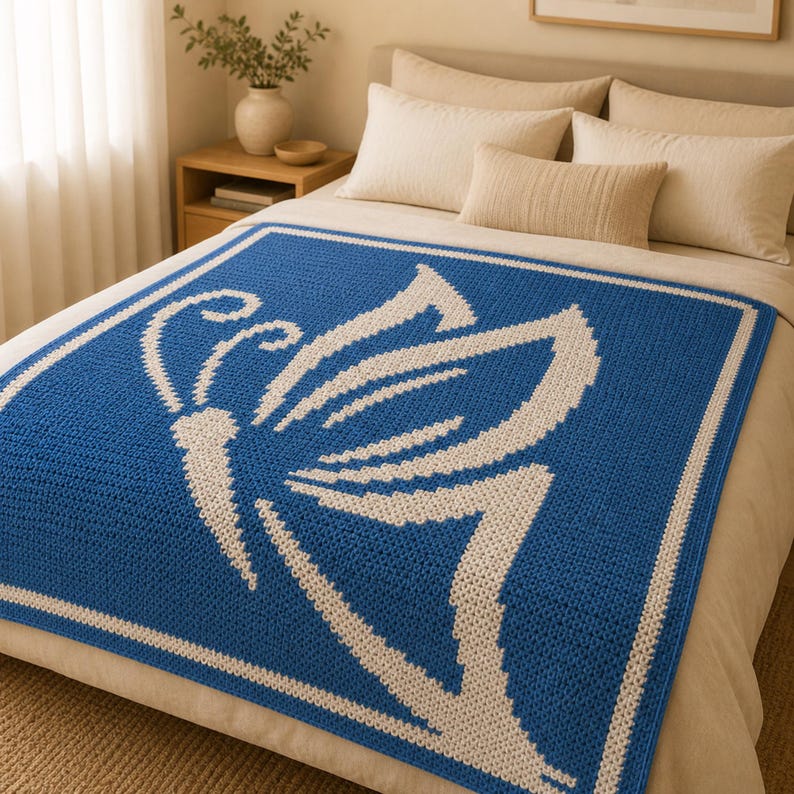 May include: A blue and white crochet blanket featuring a butterfly design. The square blanket has a white border and a white butterfly motif. It is displayed on a bed with white bedding and pillows.