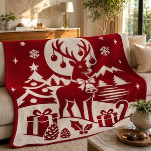 May include: A red and white knit throw blanket featuring a central reindeer design with antlers adorned with ornaments, surrounded by snowflakes, pine trees, gift boxes, and pinecones. The pattern is rendered in a two-tone colour scheme.