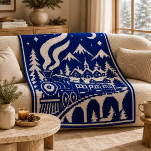 May include: A rectangular knit throw blanket featuring a two-tone blue and cream design. The pattern depicts a steam locomotive traveling across a bridge toward a village with mountains, stars, and a crescent moon in the night sky background.