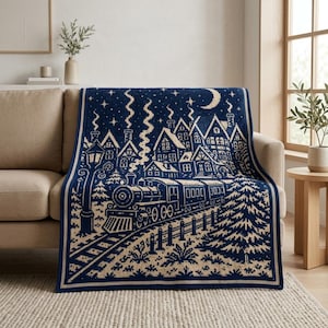 May include: A navy blue and cream knit throw blanket featuring a detailed winter scene with a steam locomotive on tracks, a row of houses with smoking chimneys, a crescent moon, stars, and evergreen trees, finished with a solid border.