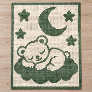 May include: A rectangular crochet blanket featuring a cream-colored background with a dark green border. The design displays a sleeping bear resting on a dark green cloud, surrounded by a dark green crescent moon and four dark green stars.
