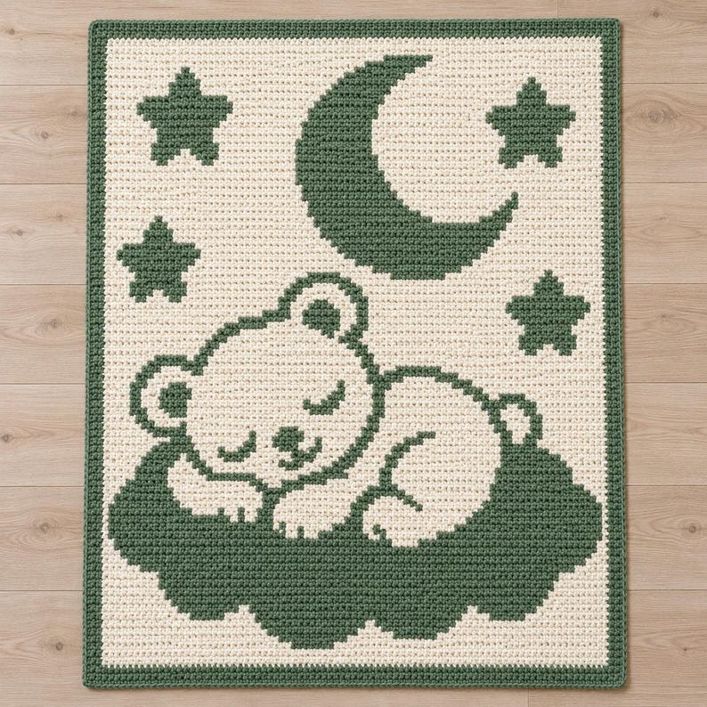 May include: A rectangular crochet blanket featuring a cream-colored background with a dark green border. The design displays a sleeping bear resting on a dark green cloud, surrounded by a dark green crescent moon and four dark green stars.