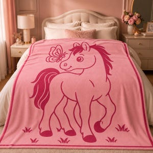 May include: A pink blanket with a cartoon horse and butterfly design. The horse is a darker shade of pink, with a flowing mane and tail. The blanket has a border and is spread over a bed.