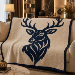 May include: A beige throw blanket with a navy blue deer head design. The blanket has a navy blue border and is draped over a beige sofa. The deer head is a detailed silhouette, adding a touch of nature-inspired decor.