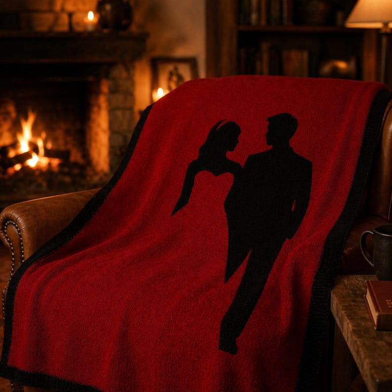 Pode incluir: Um cobertor vermelho com uma borda preta e uma silhueta de um casal. O cobertor est&aacute; sobre uma poltrona de couro marrom em frente a uma lareira. O casal &eacute; retratado em trajes formais.