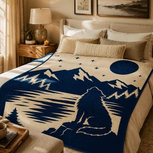 May include: A woven throw blanket featuring a dark blue and cream graphic design of a wolf howling at a full moon above a mountain range and pine forest. The scene includes a starry sky and is displayed spread across a bed with neutral bedding.