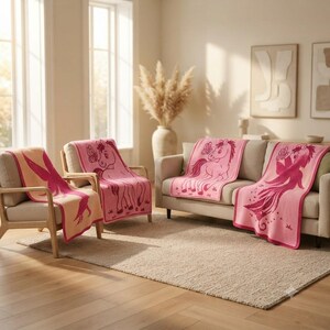 May include: A collection of soft knit blankets featuring pink and peach color palettes with repeating graphic illustrations of ponies and butterflies. The blankets are draped over a wooden armchair and a beige sofa, showcasing detailed woven patterns.