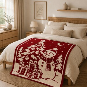 May include: A rectangular throw blanket featuring a deep red and cream color scheme with a knitted pattern of a snowman, a decorated Christmas tree, wrapped gift boxes, stars, and a crescent moon, displayed spread across a neutral-toned bed.