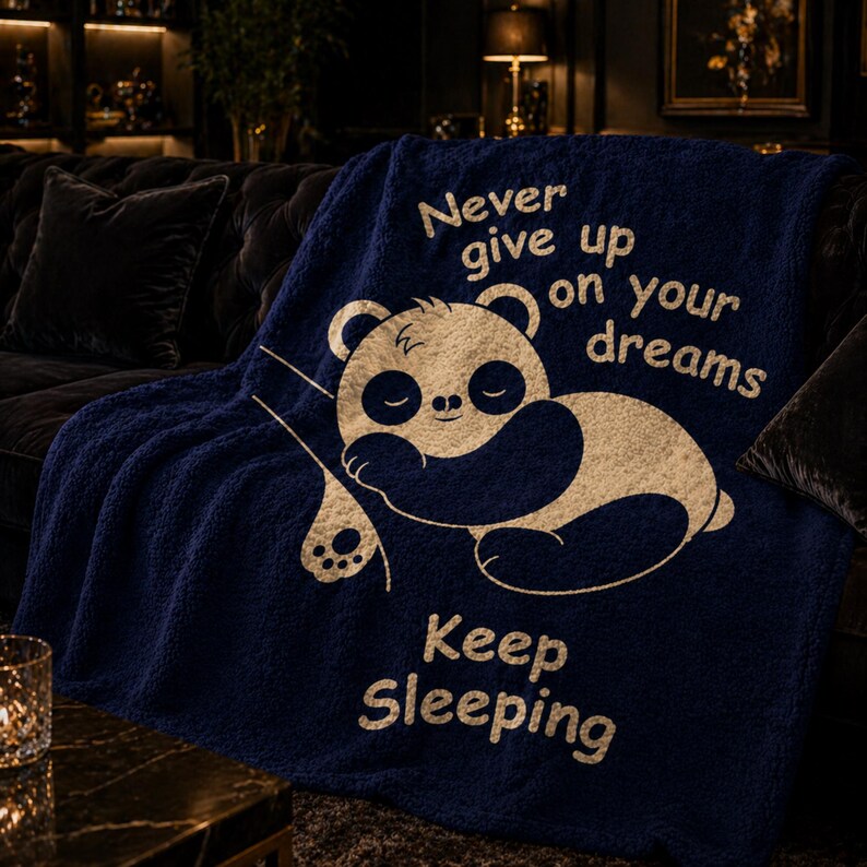 May include: A navy blue throw blanket featuring a sleeping panda bear design and the text "Never give up on your dreams" and "Keep Sleeping" in white. The blanket is made of a soft, plush material.