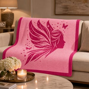 May include: A rectangular crochet blanket featuring a two-tone pink design. The center displays a dark pink silhouette of a fairy profile with large wings, surrounded by small star and butterfly motifs, framed by a solid dark pink border.