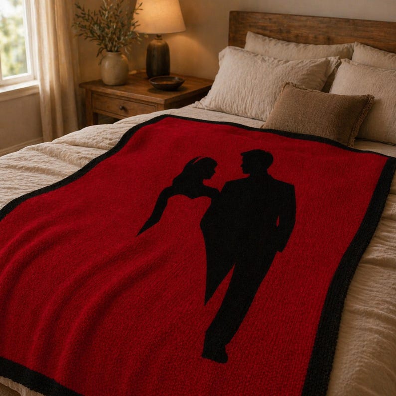 Pode incluir: Um cobertor vermelho com uma borda preta e uma silhueta preta de um casal. O cobertor est&aacute; em uma cama com roupa de cama de cores neutras. A silhueta mostra uma pessoa em um vestido e uma pessoa em um terno.