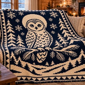May include: A dark navy blue and cream-colored knit blanket featuring a central owl perched on a pine branch. The design includes surrounding pine trees, falling snowflakes, and a decorative geometric border pattern throughout.