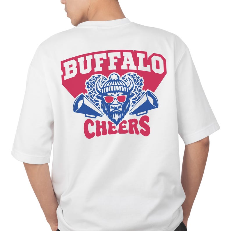 May include: White t-shirt with a graphic design on the back. The design features the word "BUFFALO" in red, a blue and white bull wearing sunglasses and a hat, and the word "CHEERS" in red, with two blue megaphones.