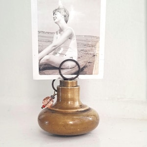 May include: A brass door knob repurposed as a photo holder with a circular metal wire loop on top. A black and white vintage photograph of a person sitting on a beach is held in the loop. A small decorative charm with a peach bead hangs from the side.