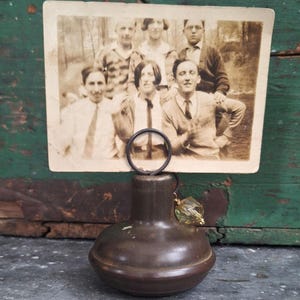 May include: A vintage photo holder with a sepia-toned photograph of a group of people. The holder is a dark brown, bulbous shape with a circular wire to hold the photo. A decorative green and gold crystal hangs from the holder.