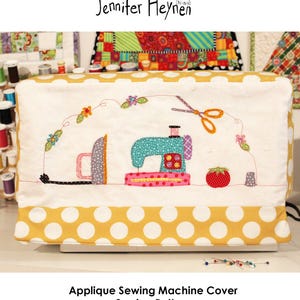 May include: Applique sewing machine cover sewing pattern. The cover features a white background with a yellow polka dot trim. The applique design includes a sewing machine, iron, scissors, and a tomato.