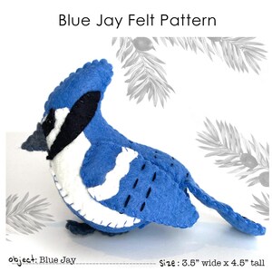Peut inclure: Un patron de geai bleu en feutre fait à la main. L'oiseau en feutre est bleu avec des accents noirs et blancs. Le texte "Blue Jay Felt Pattern" est en haut. L'oiseau en feutre mesure 8,9 cm de large et 11,4 cm de haut.