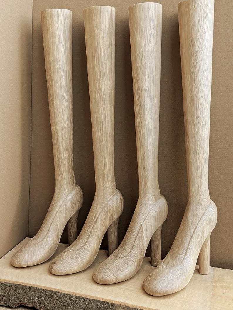 May include: Four tall, light-colored wooden leg forms shaped like high-heeled shoes. Each piece features a smooth, natural wood grain texture, a rounded toe, a sturdy block heel, and a long, slender calf section extending upward in a vertical line.