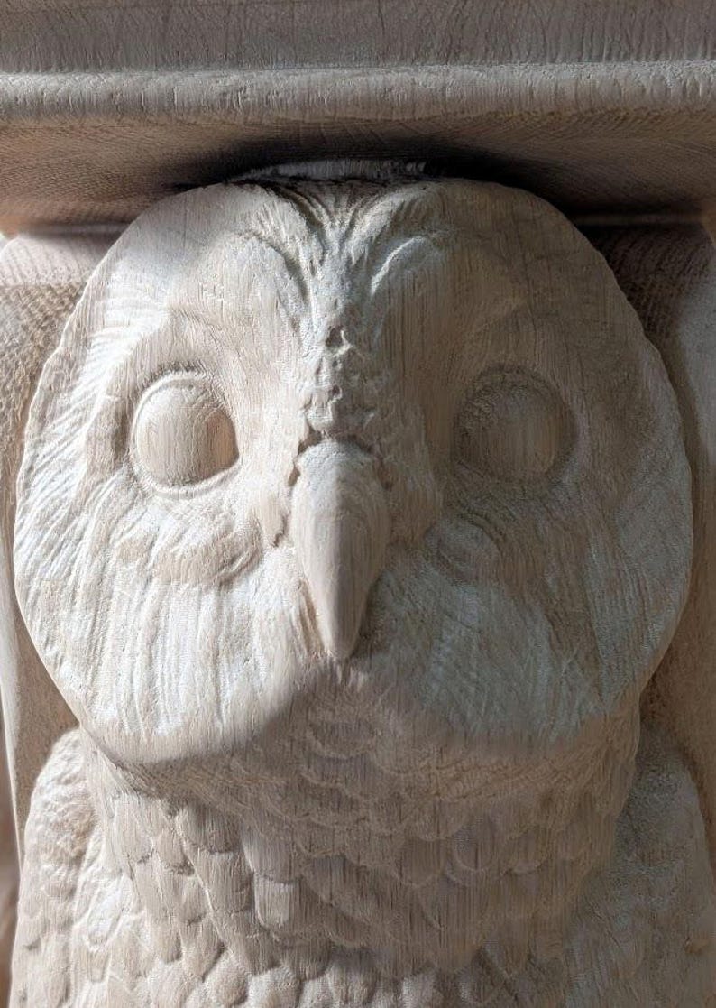 Op de afbeelding: Close-up van een houten uilensculptuur met gedetailleerde houtsnijwerk. De ogen van de uil zijn groot en rond, en zijn snavel is puntig. Het beeld is gemaakt van licht hout en heeft een gladde afwerking.