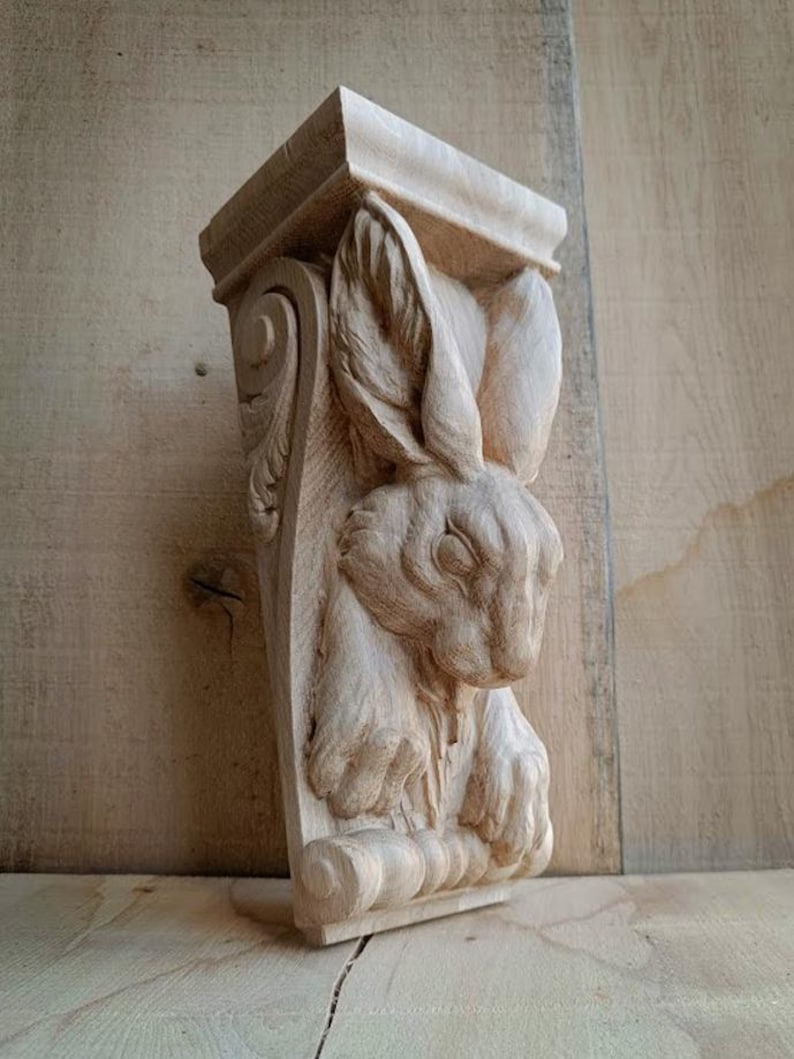 May include: A wooden corbel with a carved rabbit design. The corbel is rectangular, with a decorative top and bottom. The rabbit is carved in detail. The wood is a natural, light brown colour, and the corbel is suitable for interior decor.