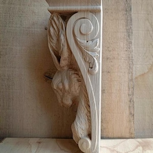 May include: A carved wooden corbel depicting a rabbit head and decorative foliage. The corbel is made from light-coloured wood and features a detailed, three-dimensional design. The rabbit's head is on the left, with leaves and a scroll design on the right.