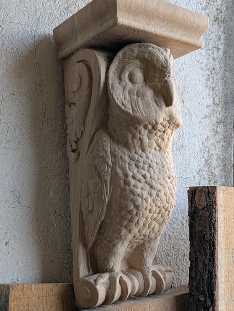 Op de afbeelding: Een houten uilensculptuur met ingewikkelde details, gesneden in een realistische stijl. De uil zit op een decoratieve basis met voluten. Het beeld is gemaakt van lichtbruin hout en heeft een natuurlijke afwerking.