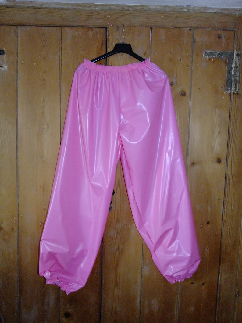 May include: Pink plastic pants with an elastic waistband and elastic cuffs at the ankles.