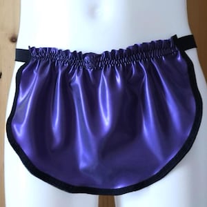 Puede incluir: Prenda morada brillante con ribete negro y cintura elástica. La tela tiene un brillo satinado y los bordes están cuidadosamente acabados con un borde negro en contraste. La prenda está diseñada para usarse alrededor de la cintura.