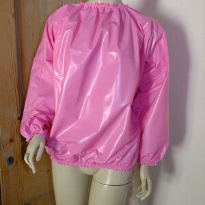 May include: A pink, shiny, long-sleeved shirt with a round neckline and elastic cuffs. The shirt is made of a smooth, water-resistant material.
