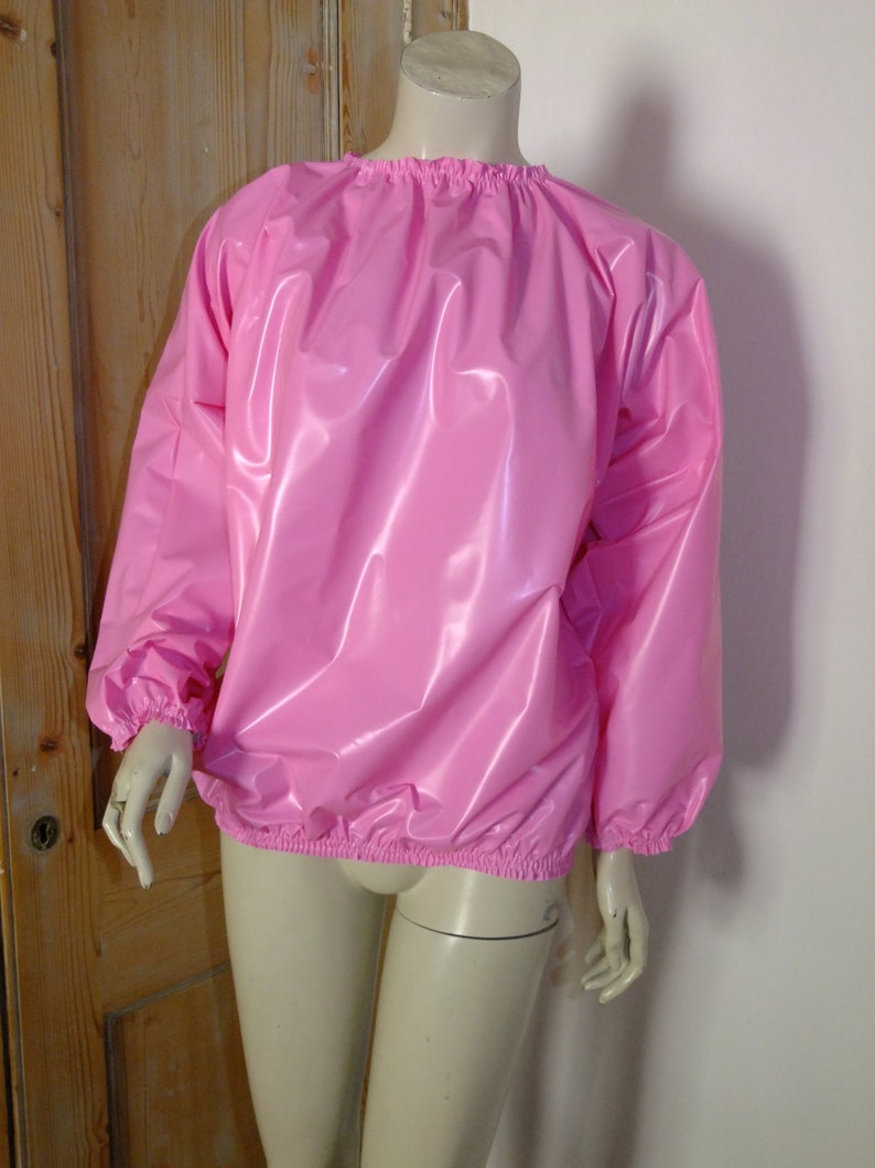 May include: A pink, shiny, long-sleeved shirt with a round neckline and elastic cuffs. The shirt is made of a smooth, water-resistant material.