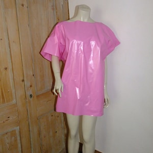 Puede incluir: Un vestido rosa brillante de manga corta hecho de vinilo. El vestido está en un maniquí.