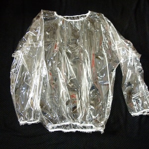 May include: A clear plastic smock with white elastic around the neck and wrists. The smock is designed to protect clothing from spills or stains.