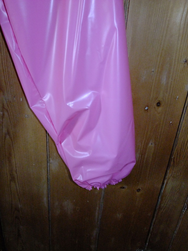 May include: A pink plastic garment with a ruffled edge. The garment is hanging on a wooden surface.