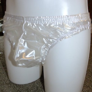 May include: Clear, plastic underwear with an elastic waistband. The underwear is displayed on a white mannequin. The material appears to be waterproof and slightly translucent.