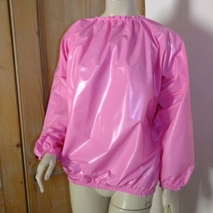 May include: A pink, shiny, long-sleeved shirt with a gathered neckline and elastic cuffs. The shirt is made of a smooth, water-resistant material.