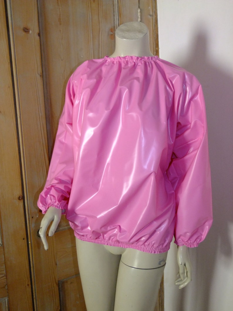 May include: A pink, shiny, long-sleeved shirt with a gathered neckline and elastic cuffs. The shirt is made of a smooth, water-resistant material.