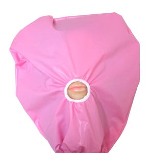 May include: A pink plastic face shield with a circular aperture displaying a pair of lips. The shield is gathered at the base and seems designed to cover the head and face.