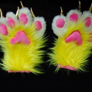 May include: A pair of yellow furry paw hand warmers with pink paw pads and gold claws.