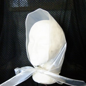 May include: A white satin bonnet with a ribbon tied at the front. The bonnet is trimmed with a white satin edge.