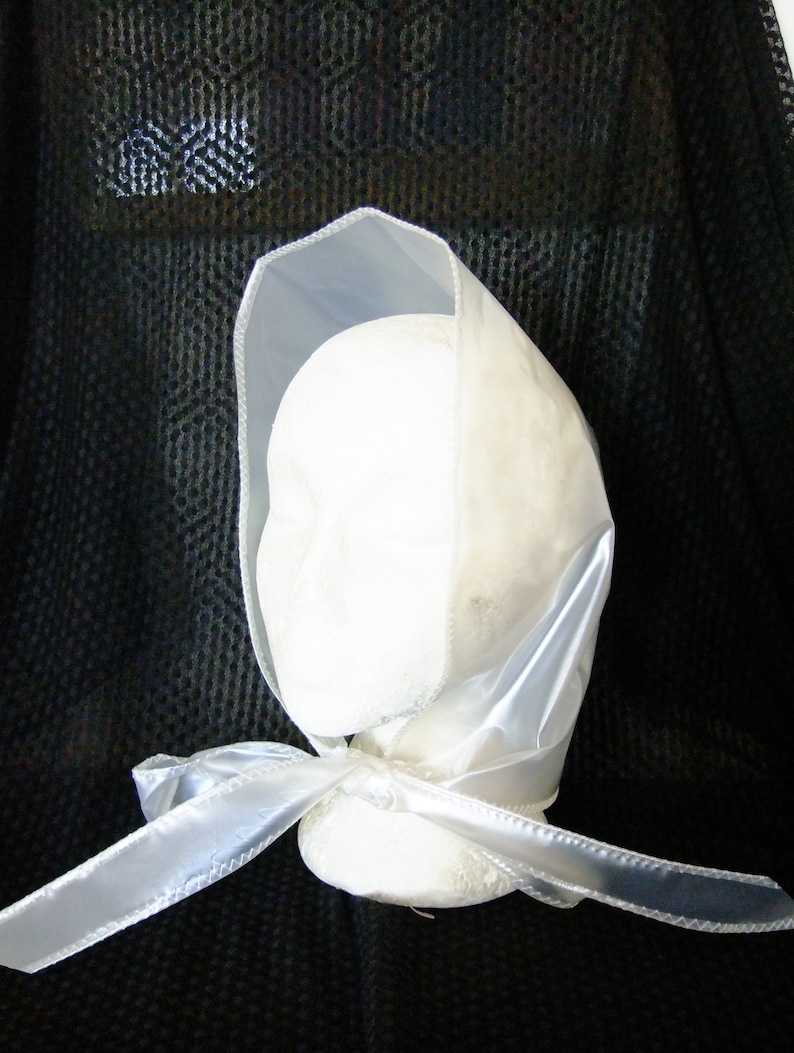 May include: A white satin bonnet with a ribbon tied at the front. The bonnet is trimmed with a white satin edge.