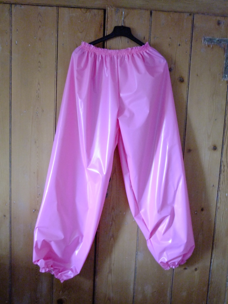 May include: Pink shiny pants with a gathered elastic waistband and gathered cuffs. The pants are made of a smooth, shiny fabric.
