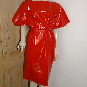 K&ouml;nnte beinhalten: Ein rotes, gl&auml;nzendes, kurz&auml;rmeliges Kleid mit einem Bindeg&uuml;rtel. Das Kleid ist aus einem glatten, gl&auml;nzenden Material.