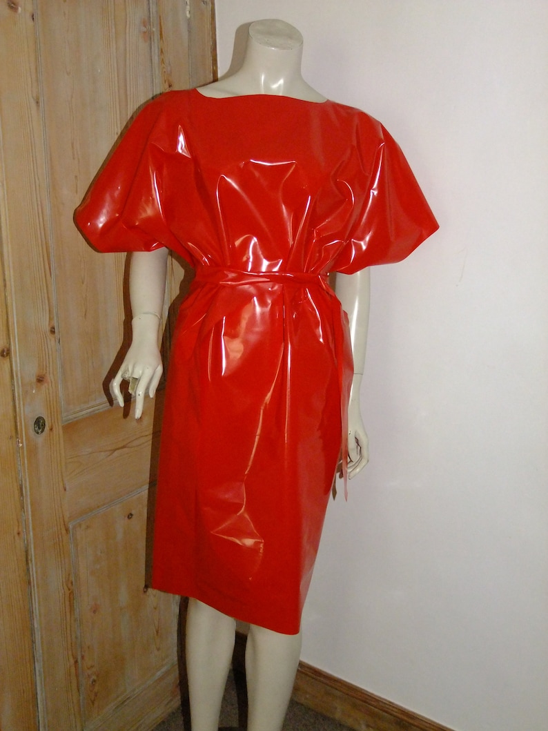 K&ouml;nnte beinhalten: Ein rotes, gl&auml;nzendes, kurz&auml;rmeliges Kleid mit einem Bindeg&uuml;rtel. Das Kleid ist aus einem glatten, gl&auml;nzenden Material.
