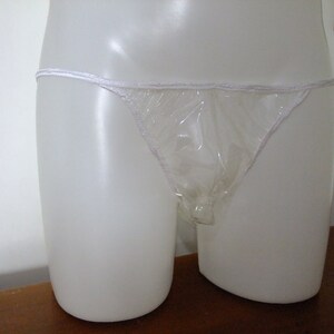 May include: A clear plastic disposable underwear garment. The garment is white and has a thin white elastic band at the top.