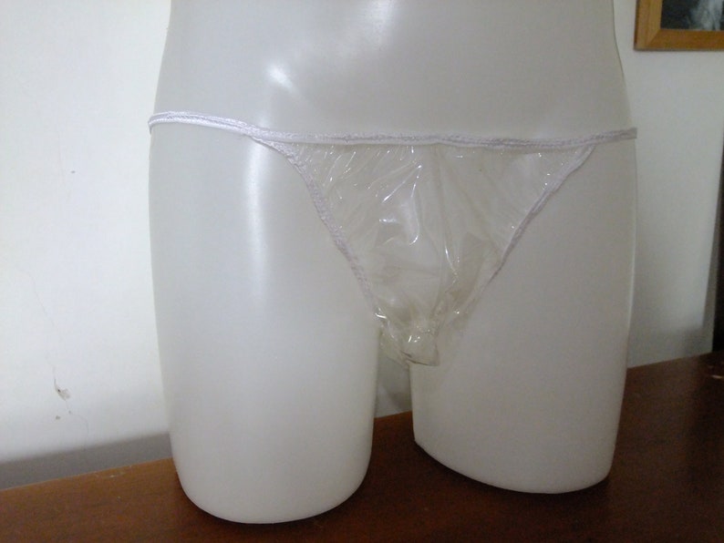 May include: A clear plastic disposable underwear garment. The garment is white and has a thin white elastic band at the top.