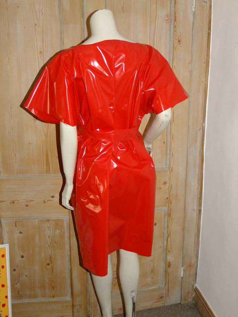 K&ouml;nnte beinhalten: Ein rotes, gl&auml;nzendes, kurz&auml;rmeliges Kleid mit einem runden Ausschnitt und einem G&uuml;rtel.